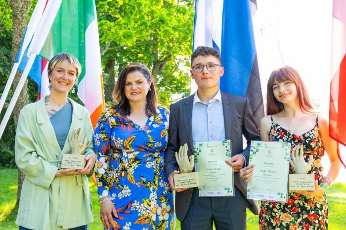 4 people standing outside holding awards