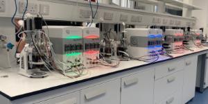 A series of bioreactors on a lab bench in the Bioprocess Innovation Suite. The reactors are lit red, green or blue depending on the status of the experiemnt.
