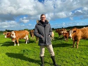 Cathal Irwin pictured on farm with cattle on grass in background