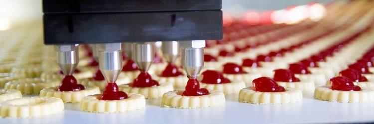 Automated production line depositing red fruit jam onto cookies