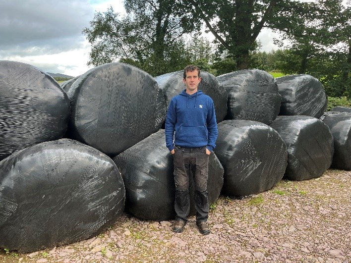 Shane Cranny standing in front of bales of silage
