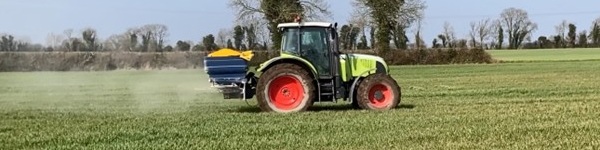 Tractor and fertiliser spreader working in a field of winter wheat