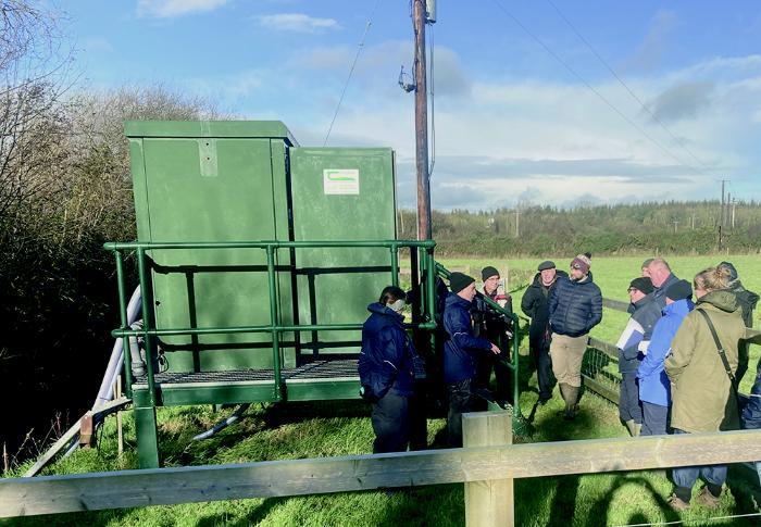 A group standing in a field visiting one of the ACP water-monitoring stations