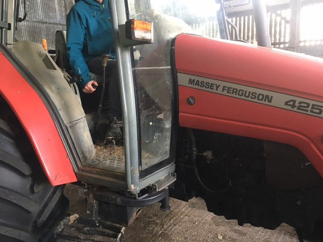 Photo of a farmer in a tractor. He is holding the handbrake.