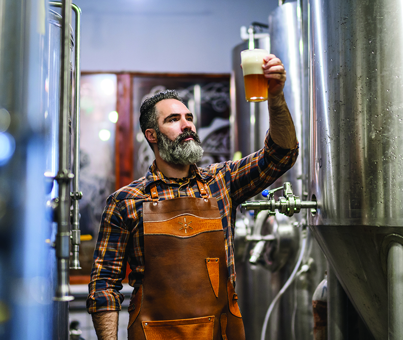 A brew master examines a pint of beer by holding it up to the light