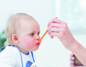 Baby with a plastic spoon on his mouth in living room